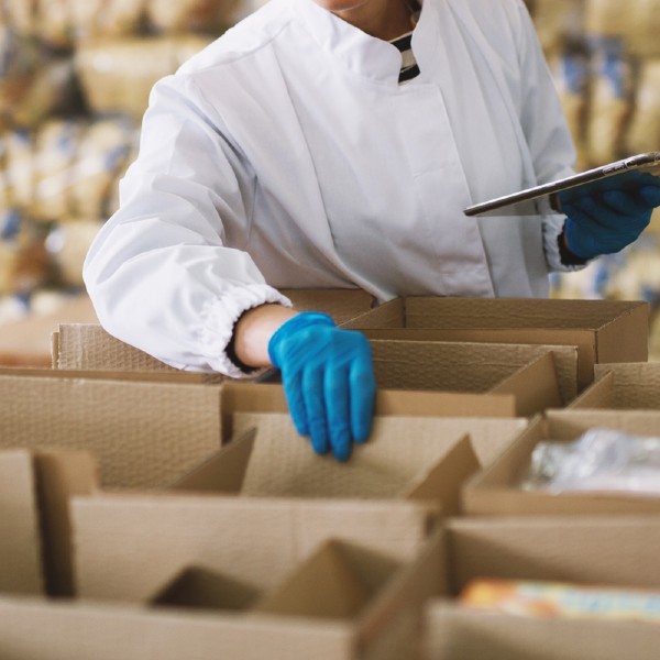Young employee in sterile clothes is checking packages ready to be delivered.